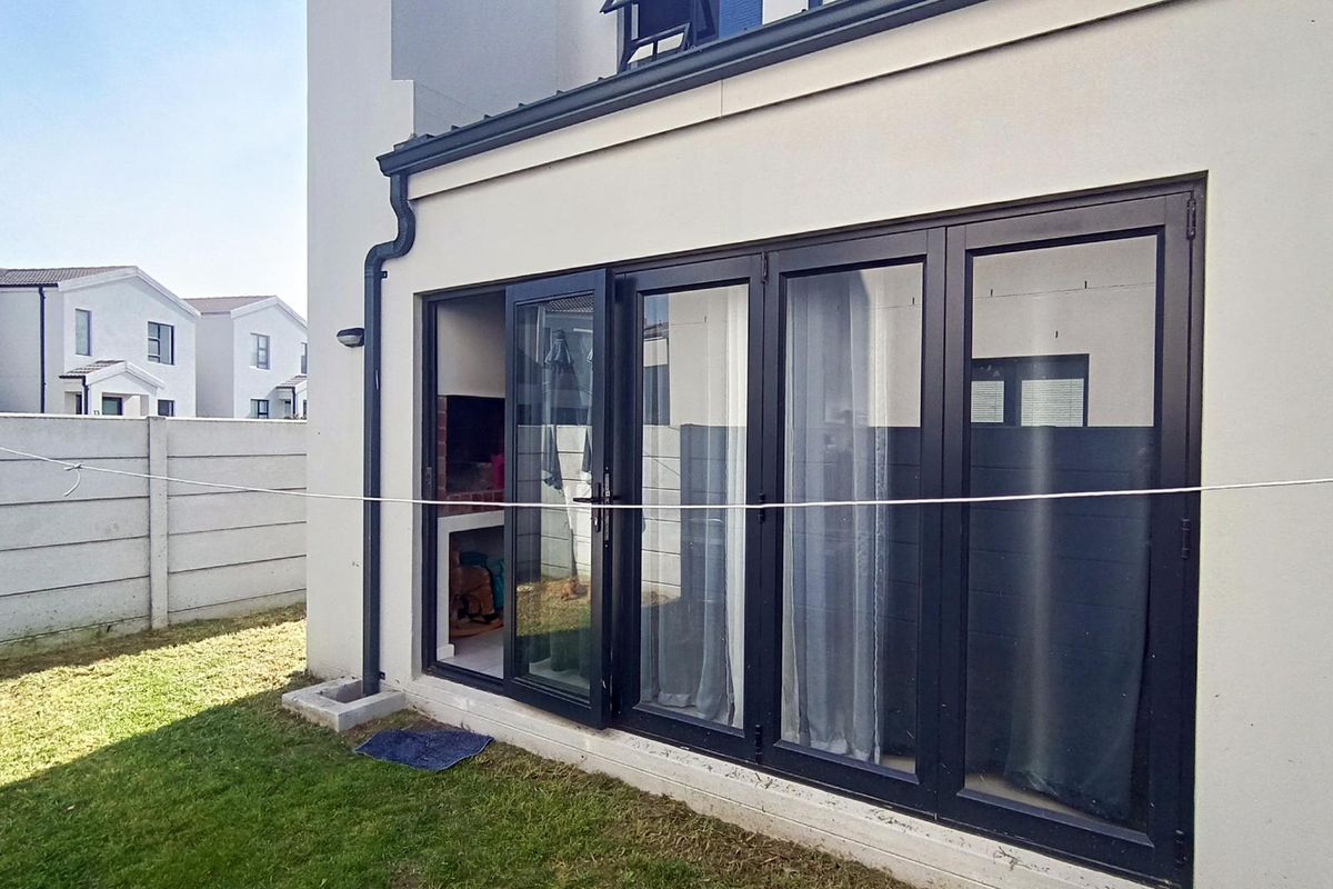 Rear view of the property featuring modern black bi-fold doors leading to an outdoor area with a built-in braai and garden space.