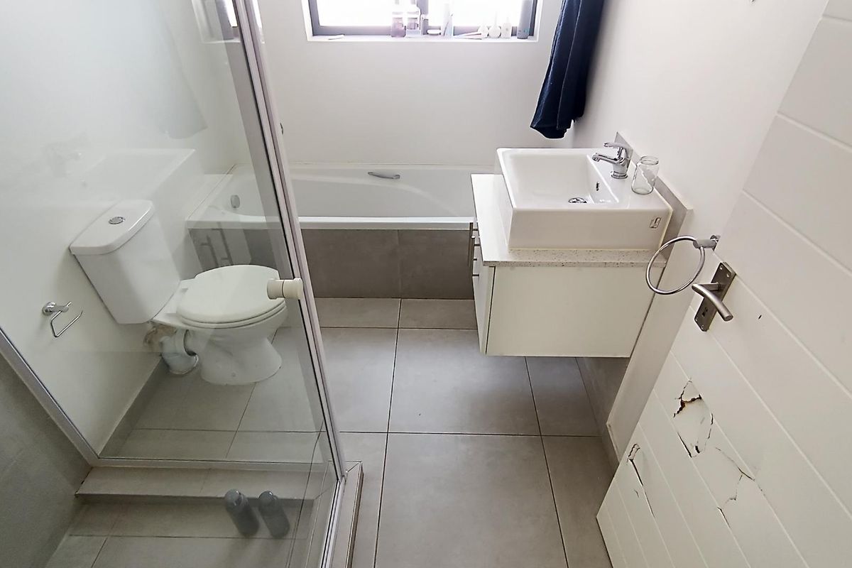 A functional bathroom featuring a shower enclosure, bathtub, wall-mounted vanity with basin, and tiled flooring. The door shows visible surface damage.