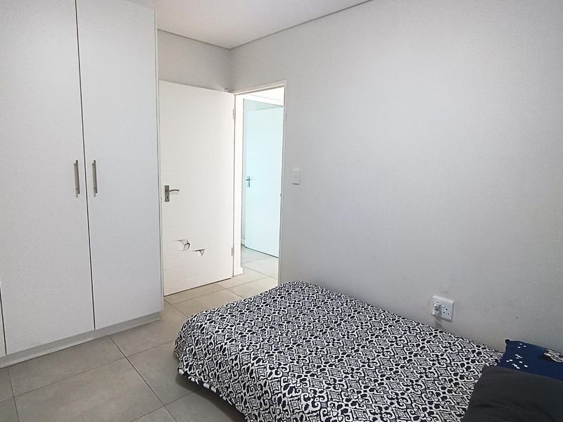 A functional bedroom featuring neutral tiled flooring, built-in cupboards, and direct access to an adjoining hallway.