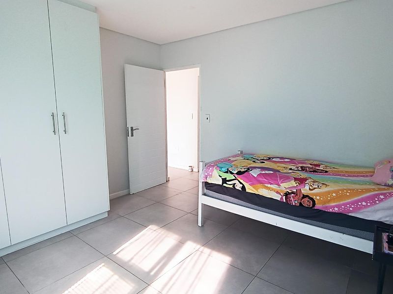 A bright bedroom featuring neutral tiled flooring and a large built-in wardrobe with modern finishes.