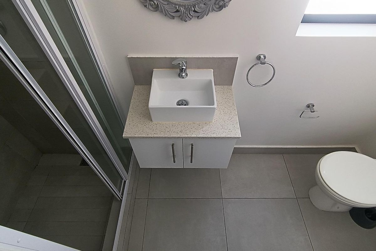 A clean, modern bathroom featuring a vanity with a basin, a glass shower enclosure, and a toilet with neutral floor tiling.