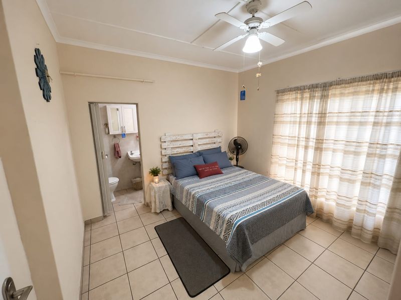 A bedroom featuring tiled flooring, a ceiling fan, and an attached en-suite bathroom accessed via a folding door.