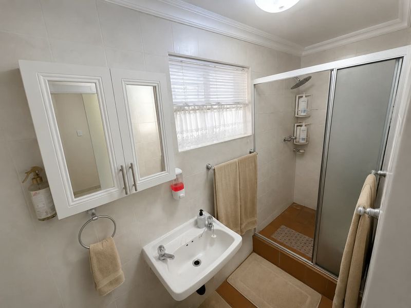 A functional bathroom featuring a wall-mounted basin, mirrored vanity cabinet, and a glass-enclosed shower with tiled finishes throughout.