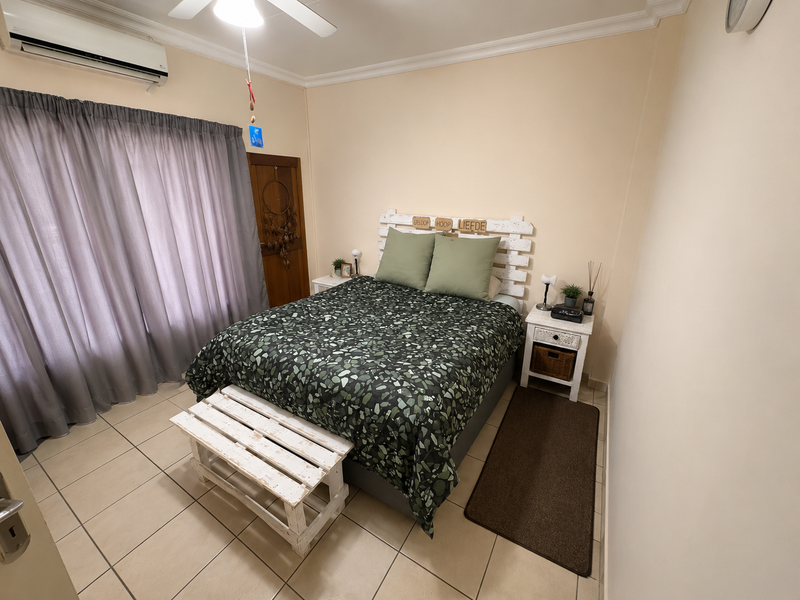 A well-maintained bedroom featuring tiled flooring, a ceiling fan, and a wall-mounted air conditioning unit.