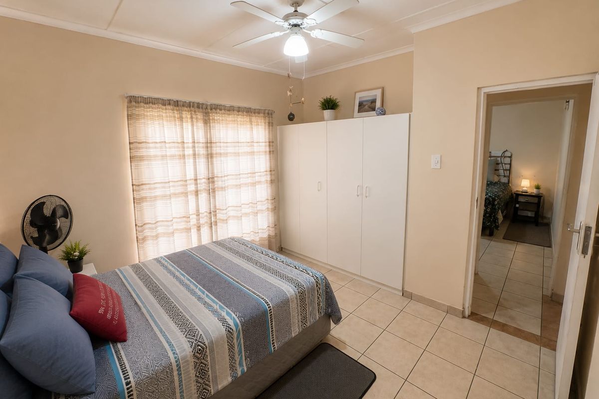 A functional bedroom featuring tiled flooring, built-in cupboards, and a ceiling fan, offering a neutral canvas for potential interior updates.