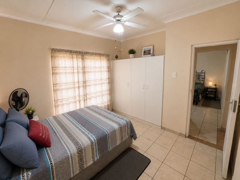 A functional bedroom featuring tiled flooring, built-in cupboards, and a ceiling fan, offering a neutral canvas for potential interior updates.