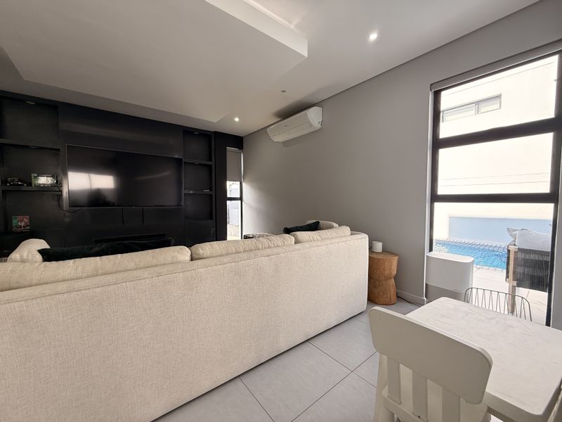 Modern living room featuring built-in cabinetry, tiled flooring, and large windows with views of the outdoor pool area.