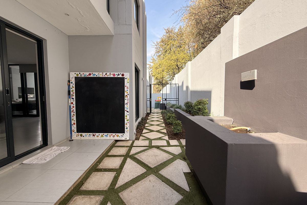 A side exterior walkway featuring paved stepping stones, a modern water feature, and sliding glass door access to the interior living space.