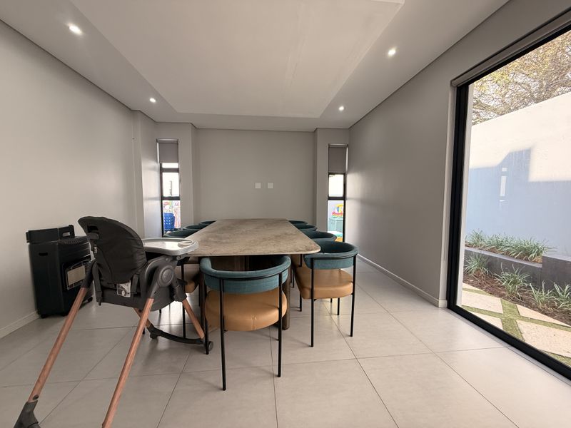 A modern dining room featuring large format floor tiles, recessed downlighting, and a large sliding glass door providing access to the outdoor area.