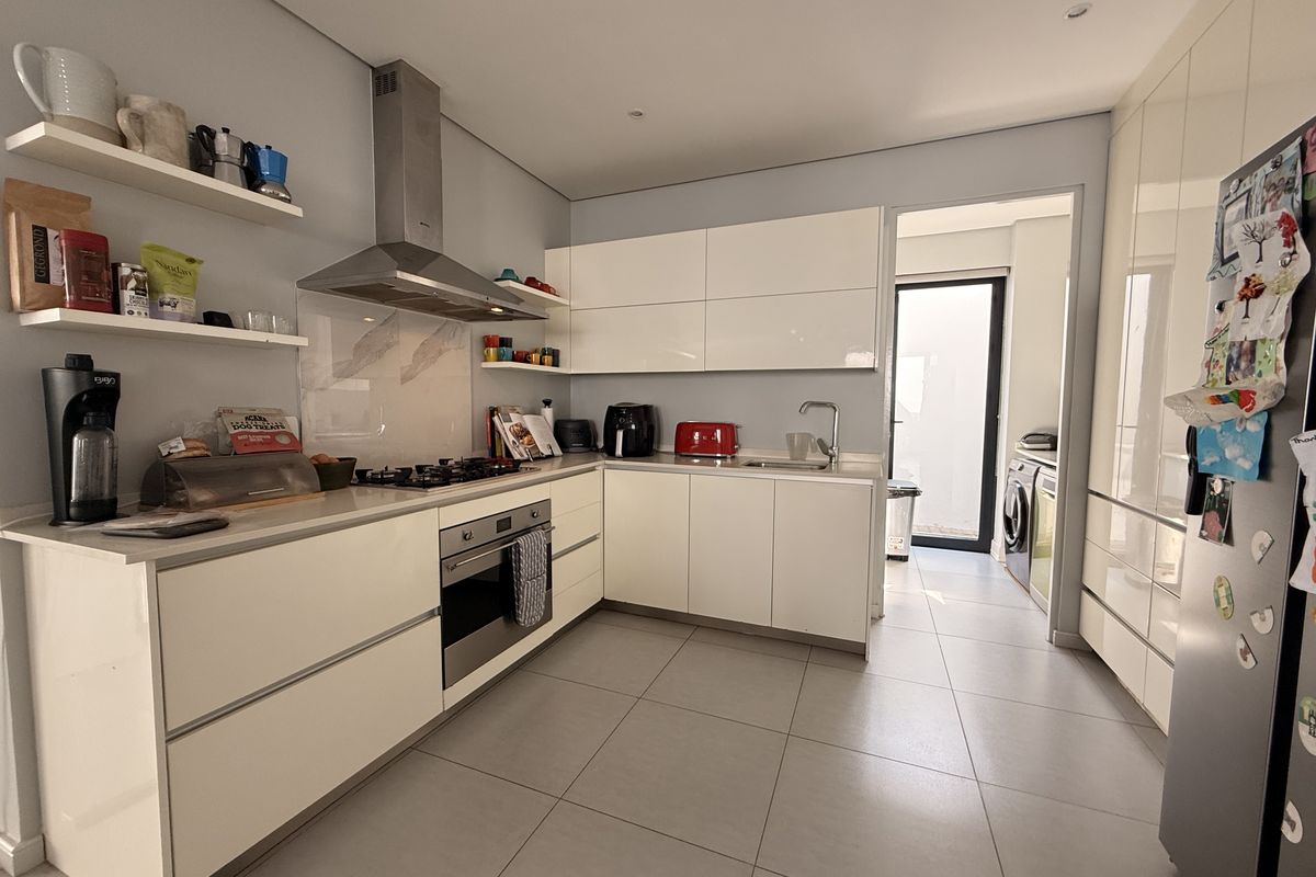 Modern kitchen featuring high-gloss white cabinetry, stone countertops, integrated stainless steel appliances, and tiled flooring, with an adjacent scullery area.