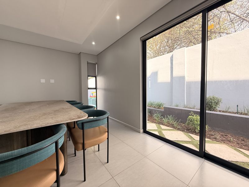 Modern dining area featuring large sliding glass doors that open to a landscaped garden, complemented by neutral tiled flooring and recessed lighting.