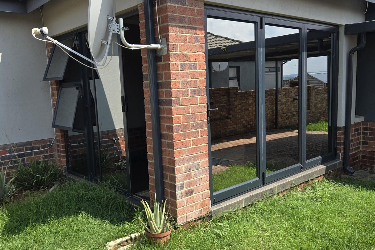 Rear exterior view of the house featuring brick detailing, modern aluminium framed glass doors, and a paved garden area.