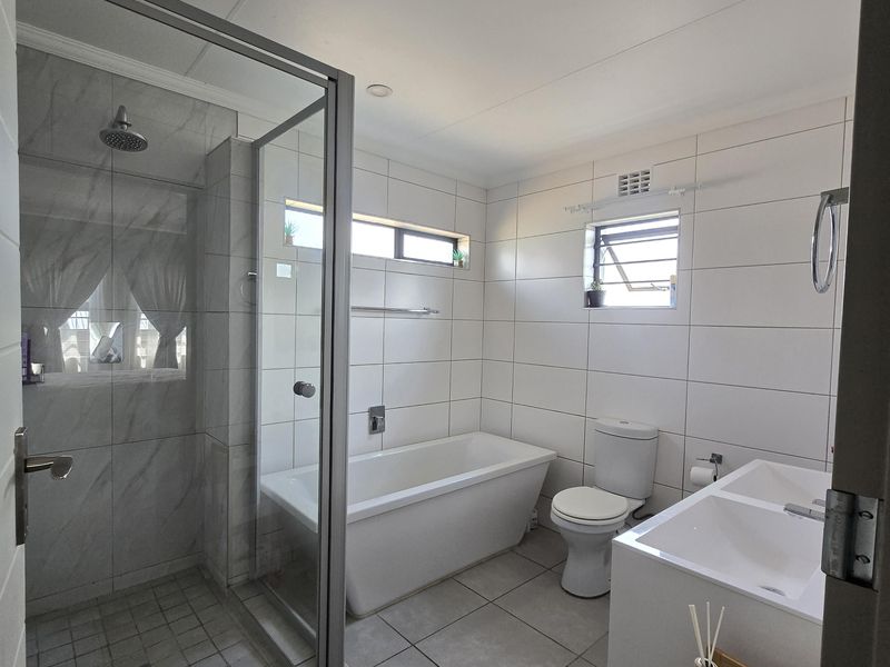 Modern bathroom featuring a glass-enclosed shower, a freestanding bathtub, and a double vanity with clean white tiling throughout.