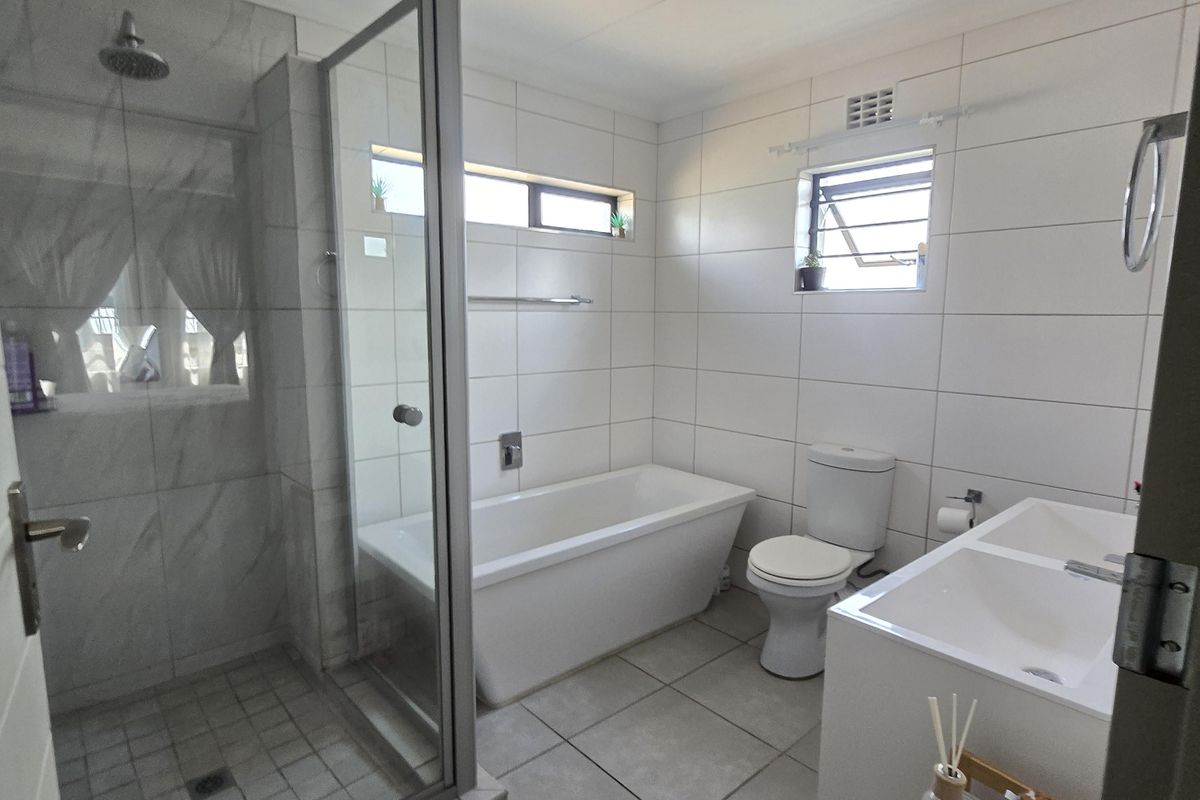 Modern bathroom featuring a glass-enclosed shower, a sleek freestanding bathtub, and a double vanity with contemporary white wall and floor tiling.