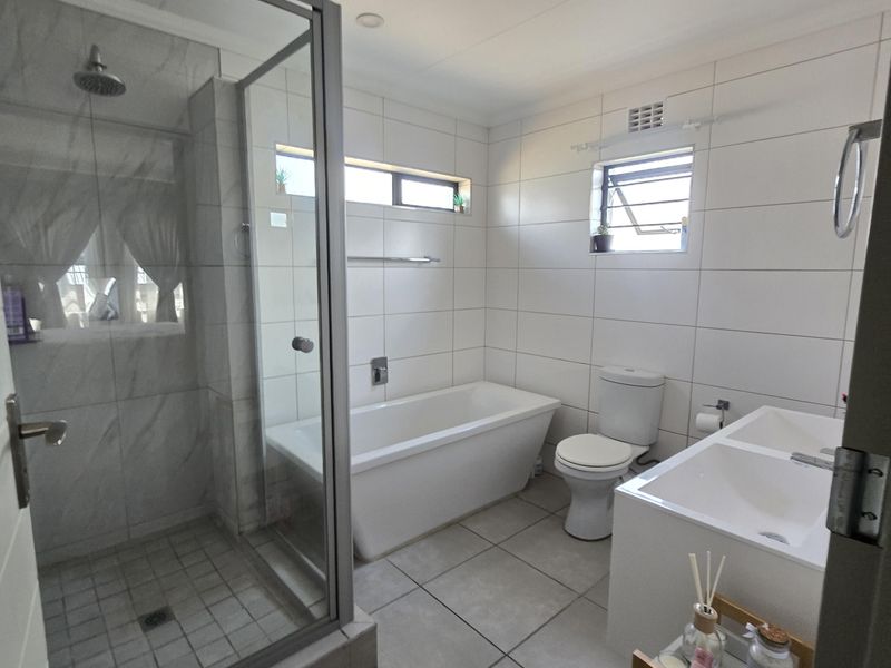 Modern bathroom featuring a glass-enclosed shower, a sleek freestanding bathtub, and a double vanity with contemporary white wall and floor tiling.