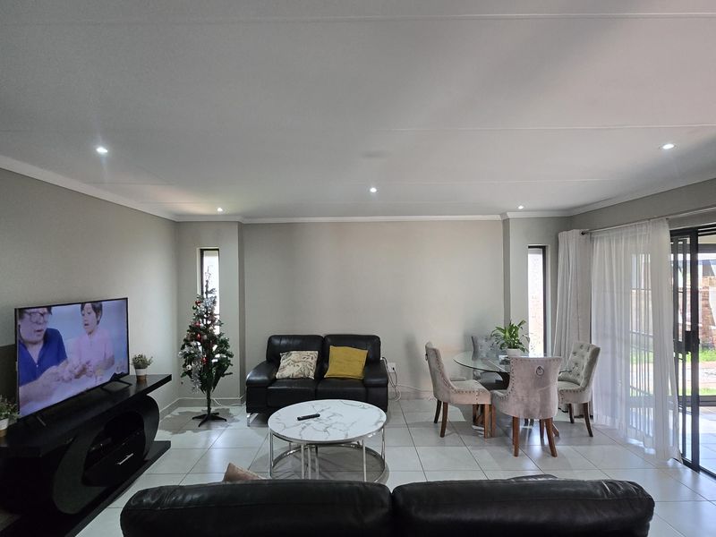 Spacious open-plan living and dining area featuring neutral walls, large format floor tiles, recessed lighting, and sliding glass doors leading to the patio.