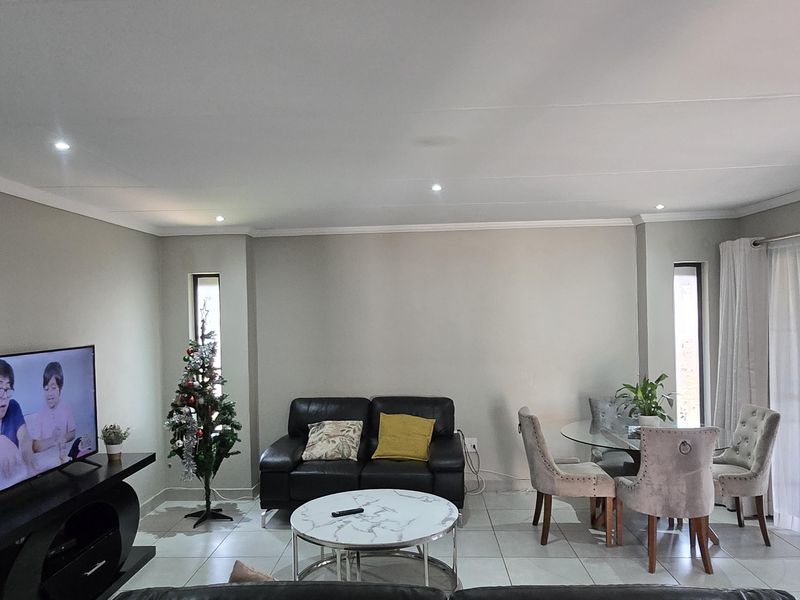 An open-plan living and dining area featuring neutral walls, tiled flooring, and recessed downlighting, creating a bright and functional space.
