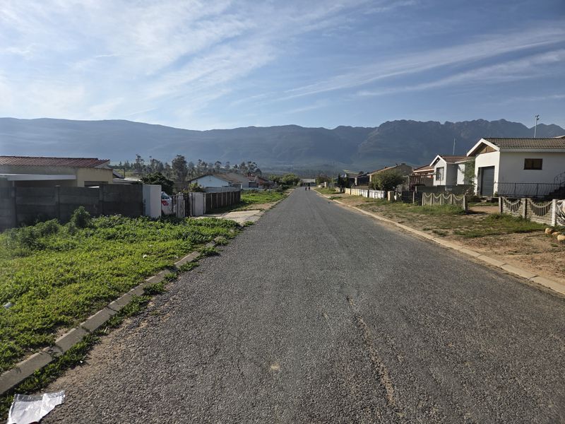 A view looking down a residential street featuring asphalt paving, concrete kerbing, and surrounding residential properties with mountain views in the background.
