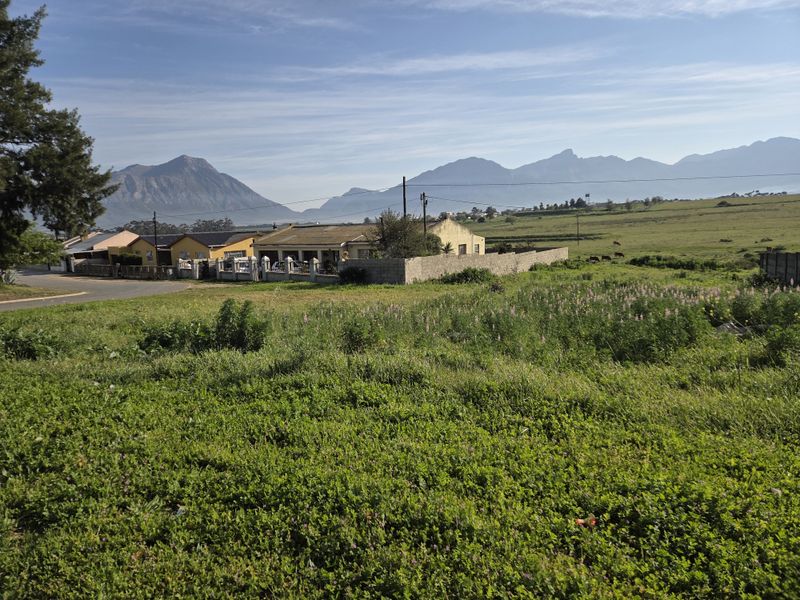 A scenic view of an open residential plot featuring expansive mountain vistas and surrounding neighborhood landscape.