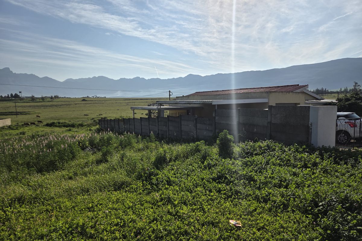 Rear view of a residential property featuring a precast boundary wall, covered patio area, and expansive mountain views over open land.