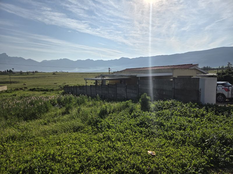 Rear view of a residential property featuring a precast boundary wall, covered patio area, and expansive mountain views over open land.