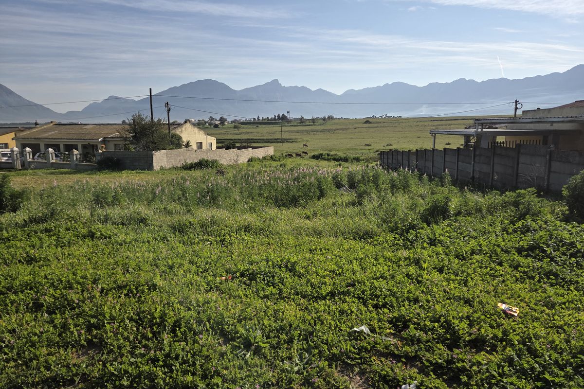 A view of a vacant residential plot featuring natural vegetation, enclosed by concrete boundary walls with scenic mountain views in the background.