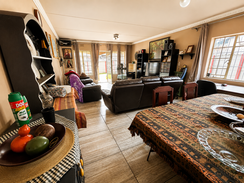 Spacious open-plan living and dining area featuring tiled flooring, decorative ceiling cornices, and natural light through security-barred windows.