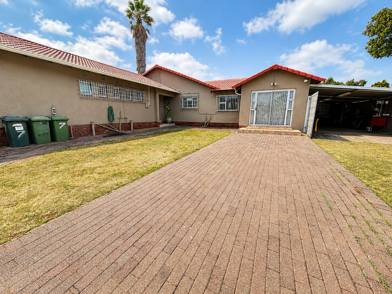 Front view of a single-story house featuring a paved driveway, tiled roof, security bars on windows, and an attached carport.