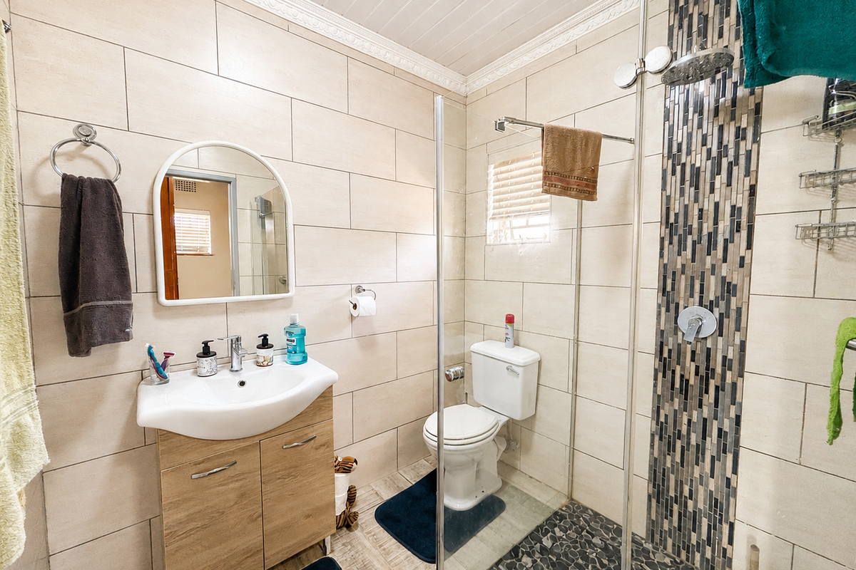 Modern bathroom featuring a vanity with basin, glass-enclosed shower with mosaic tile accent, pebble flooring, and neutral wall tiling.