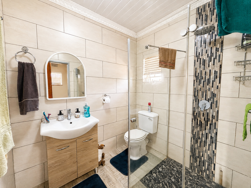 Modern bathroom featuring a vanity with basin, glass-enclosed shower with mosaic tile accent, pebble flooring, and neutral wall tiling.