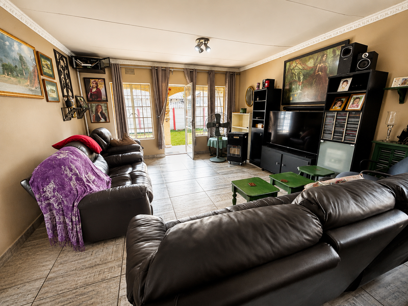 A comfortable living room featuring tiled flooring, decorative ceiling cornices, and direct access to the rear garden through a glass sliding door.