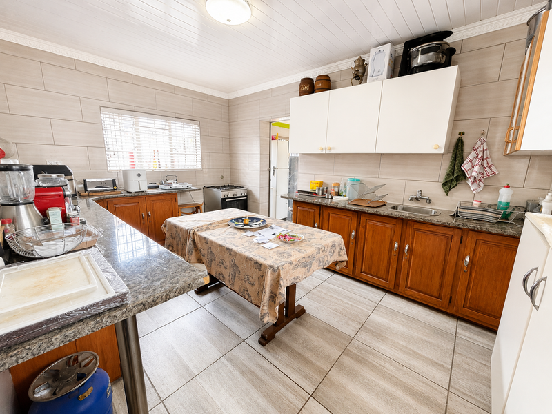 A functional kitchen featuring wooden cabinetry, granite countertops, tiled walls, and a gas stove, offering a practical layout with ample storage space.