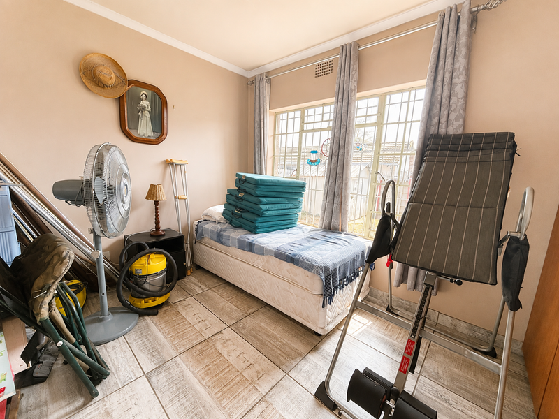 A bedroom featuring tiled flooring and large windows with security bars, providing natural light and ventilation.