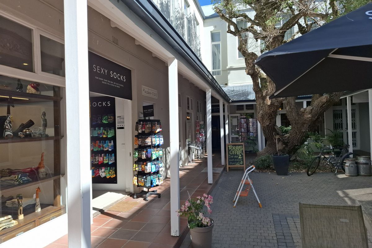 A charming outdoor courtyard area featuring a covered walkway with tiled flooring, timber support posts, and access to commercial storefronts.