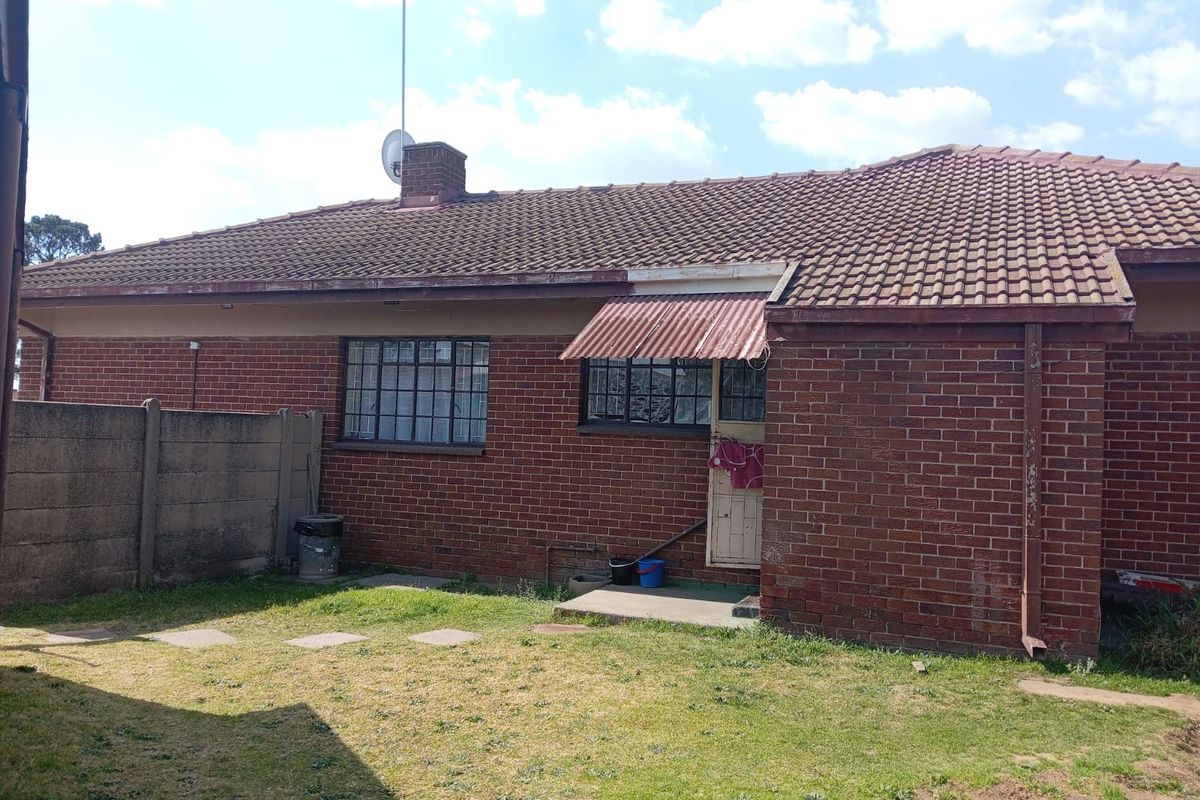 Rear view of a single-story brick house featuring a tiled roof, steel-framed windows, and a small garden area with a concrete boundary wall.