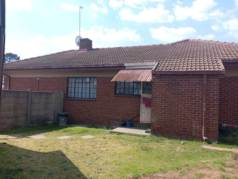 Rear view of a single-story brick house featuring a tiled roof, steel-framed windows, and a small garden area with a concrete boundary wall.