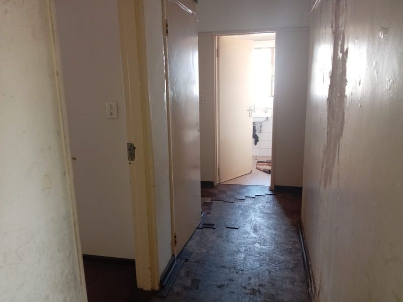 A narrow hallway featuring built-in cupboards and damaged flooring, leading towards a bathroom area. The space requires significant cosmetic repairs and refurbishment.