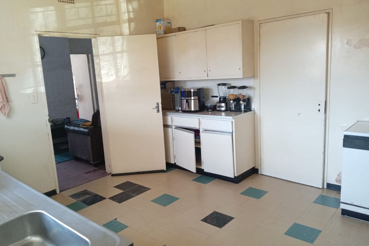 A dated kitchen featuring original built-in cabinetry, a stainless steel sink, and vinyl tile flooring, requiring cosmetic updates and repairs.