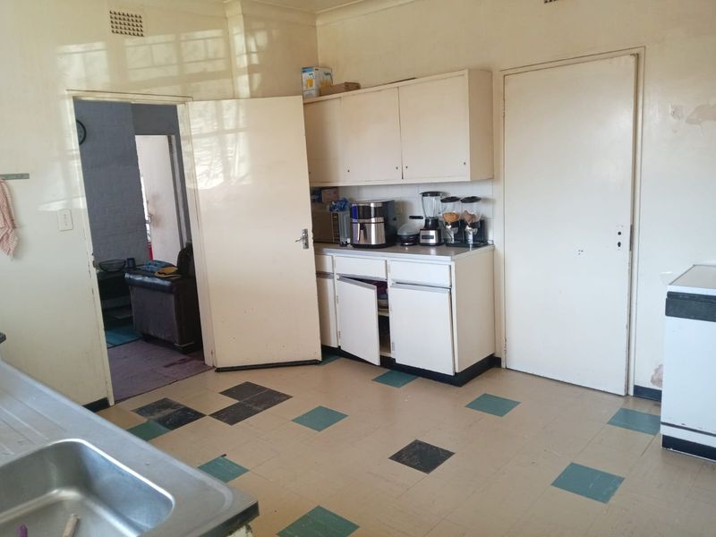 A dated kitchen featuring original built-in cabinetry, a stainless steel sink, and vinyl tile flooring, requiring cosmetic updates and repairs.