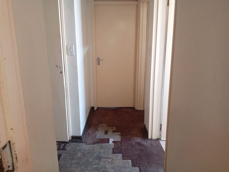A narrow interior hallway featuring damaged parquet flooring and multiple internal doors, requiring cosmetic updates to improve the overall finish.