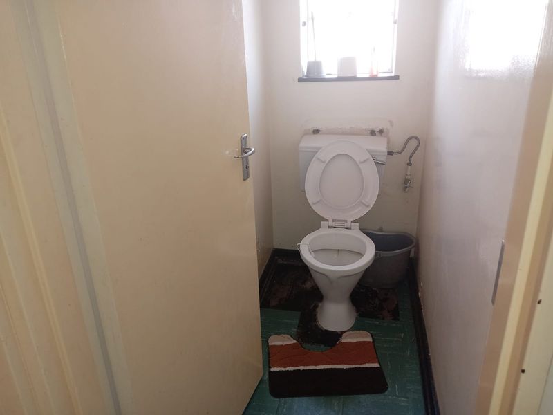A small, dated bathroom featuring a standard toilet and window, currently requiring cosmetic updates and flooring repairs.