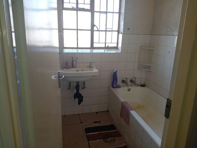A dated bathroom featuring a pedestal basin, built-in bathtub, and tiled finishes, requiring renovation to update the worn fixtures and surfaces.