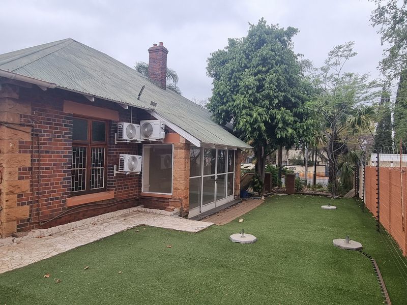 Rear exterior view of a brick house featuring a corrugated roof, artificial lawn, and perimeter security fencing with razor wire.