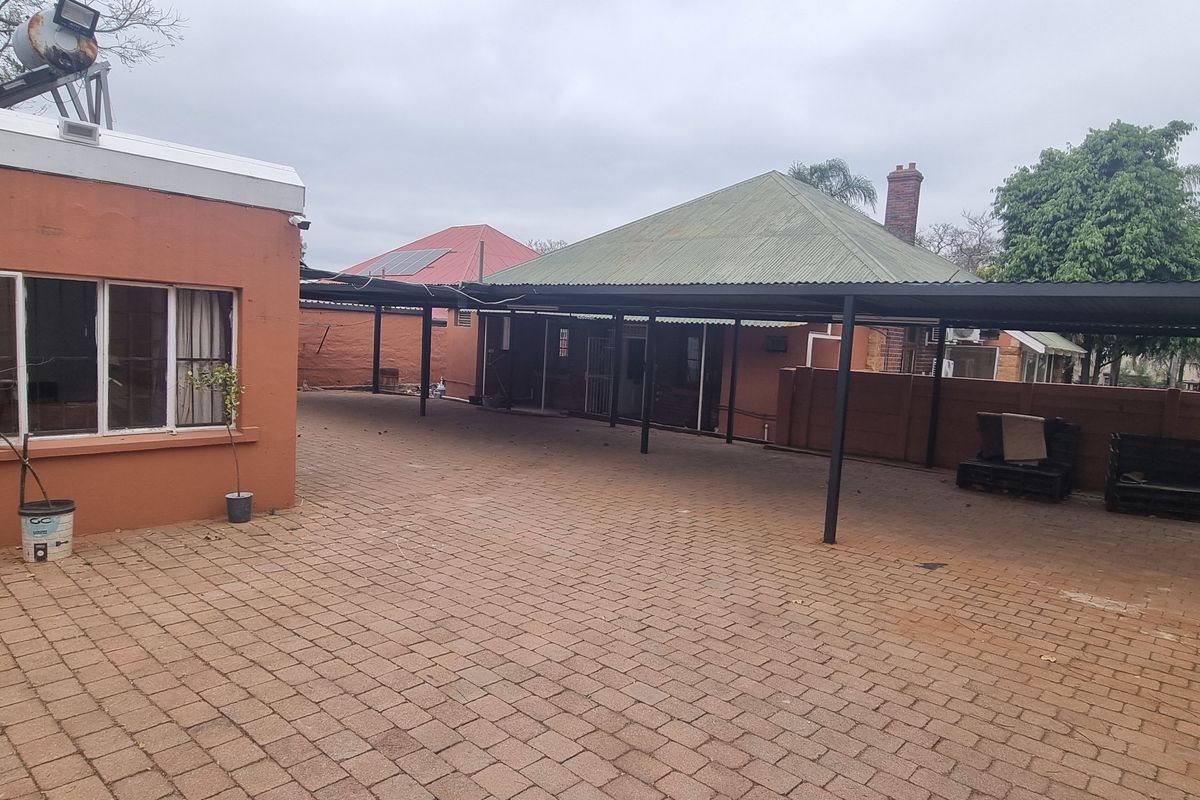 Spacious paved rear courtyard featuring a large carport structure, perimeter walling with electric fencing, and a solar water heating system.