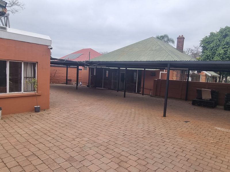 Spacious paved rear courtyard featuring a large carport structure, perimeter walling with electric fencing, and a solar water heating system.