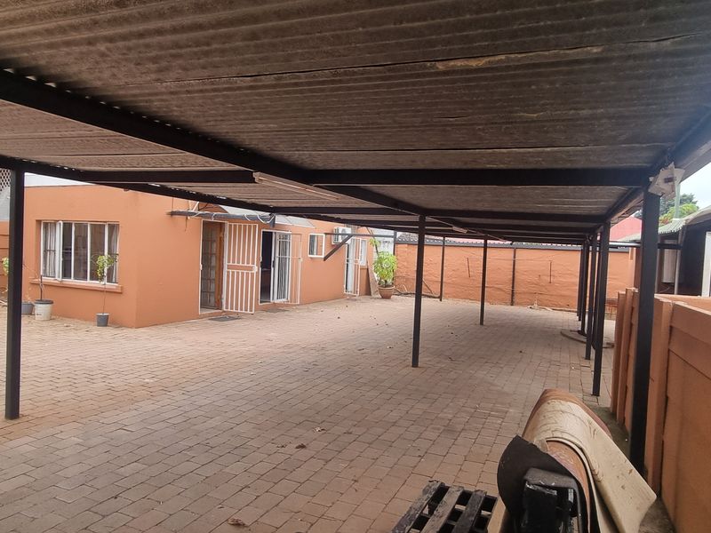 Spacious rear exterior area featuring a large covered carport, paved driveway, and secure perimeter walling.