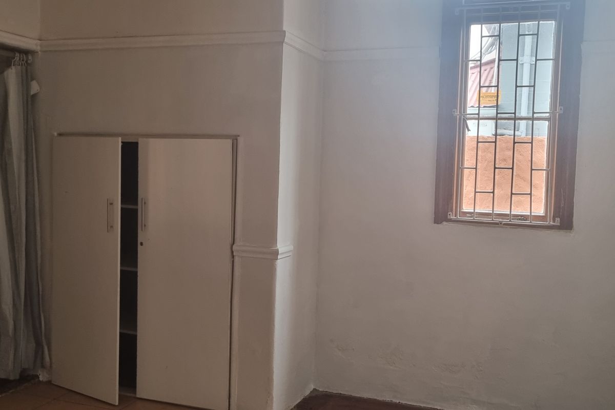 A vacant bedroom featuring a built-in cupboard, security bars on the window, and an attached en-suite bathroom with a pedestal basin and toilet.