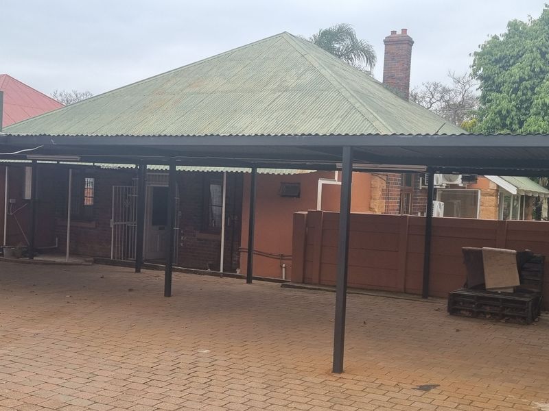 Rear exterior view featuring a large covered carport area with brick paving and a corrugated metal roof structure.
