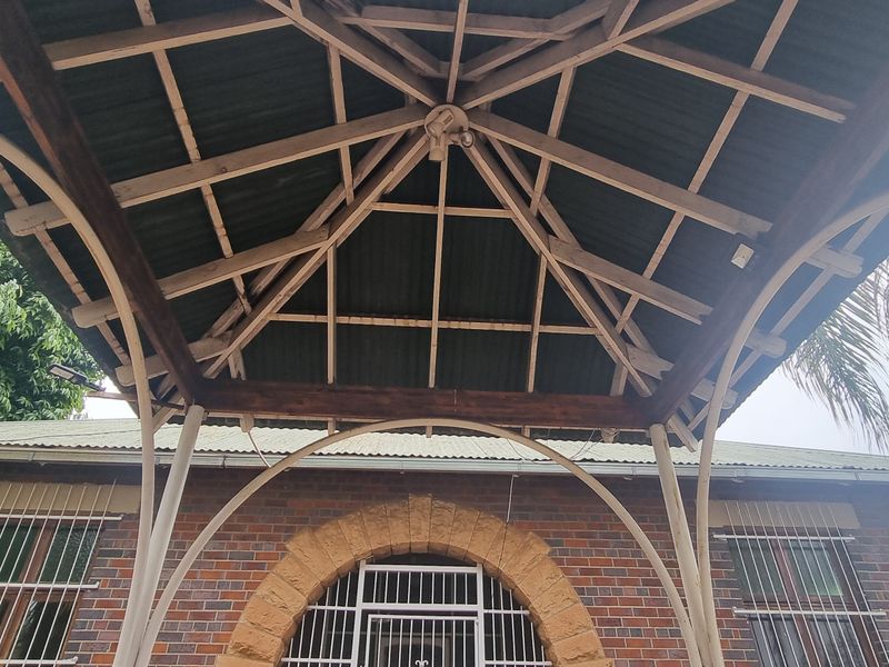 A covered outdoor patio area featuring an exposed timber truss roof structure, brick facade, and a distinctive stone archway entrance.