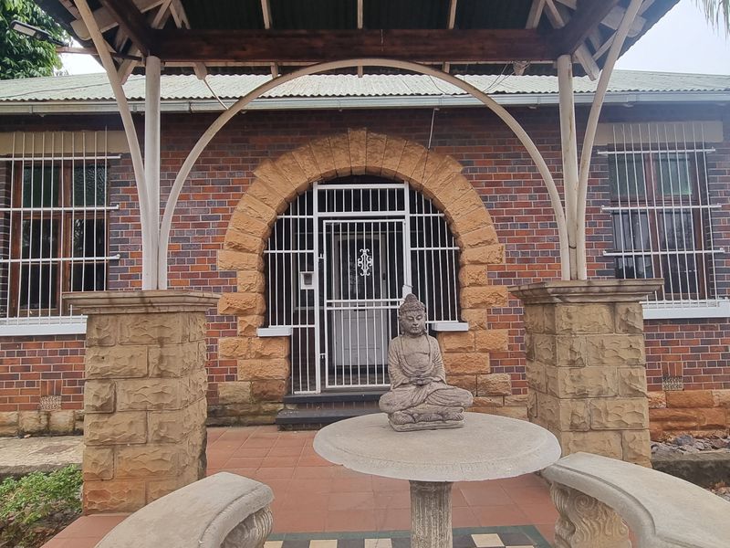 Front facade featuring classic brickwork, a distinctive stone archway entrance, and a covered patio area with security bars on windows.